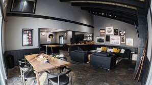 A modern living area with a stone floor, a wooden dining table with chairs, a black sofa, and a kitchen in the background.