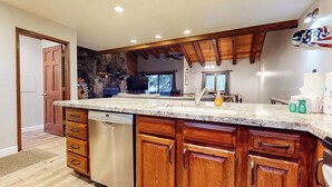A kitchen with a large island, wooden cabinets, a dishwasher, and a stone accent wall. - Mammoth Pines #02 | Year-Round Activities! (Mammoth Lakes)