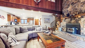 A cozy living room with a sectional sofa, a fireplace, and a kitchen in the background. - Mammoth Pines #02 | Year-Round Activities! (Mammoth Lakes)