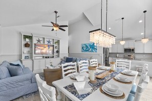 A modern kitchen with white cabinetry, a dining area with a large table set for six, and a ceiling fan. - Tiki By The Sea 5 Bedroom Home (Holmes Beach)