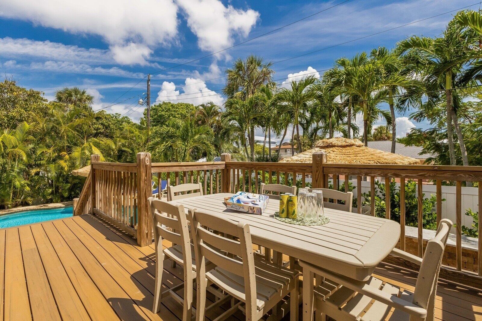 Eine Holzterrasse mit Pool, umgeben von Palmen und einer Struktur mit Reetdach.