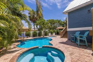 A swimming pool with a stone border, surrounded by palm trees and lounge chairs. - Tiki By The Sea 5 Bedroom Home (Holmes Beach)
