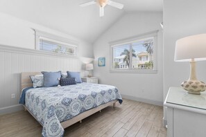 A bedroom with a bed, nightstand, lamp, and windows. - Tiki By The Sea 5 Bedroom Home (Holmes Beach)