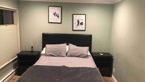 Une chambre à coucher avec un lit, deux tables de chevet, une fenêtre avec des stores et deux tableaux encadrés accrochés au mur.