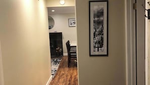 Un couloir avec un plancher en bois, un tableau encadré au mur et une porte sur la droite.