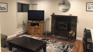 Un salon avec un téléviseur posé sur un meuble en bois, une cheminée, un ventilateur de plafond et un grand miroir accroché au mur.