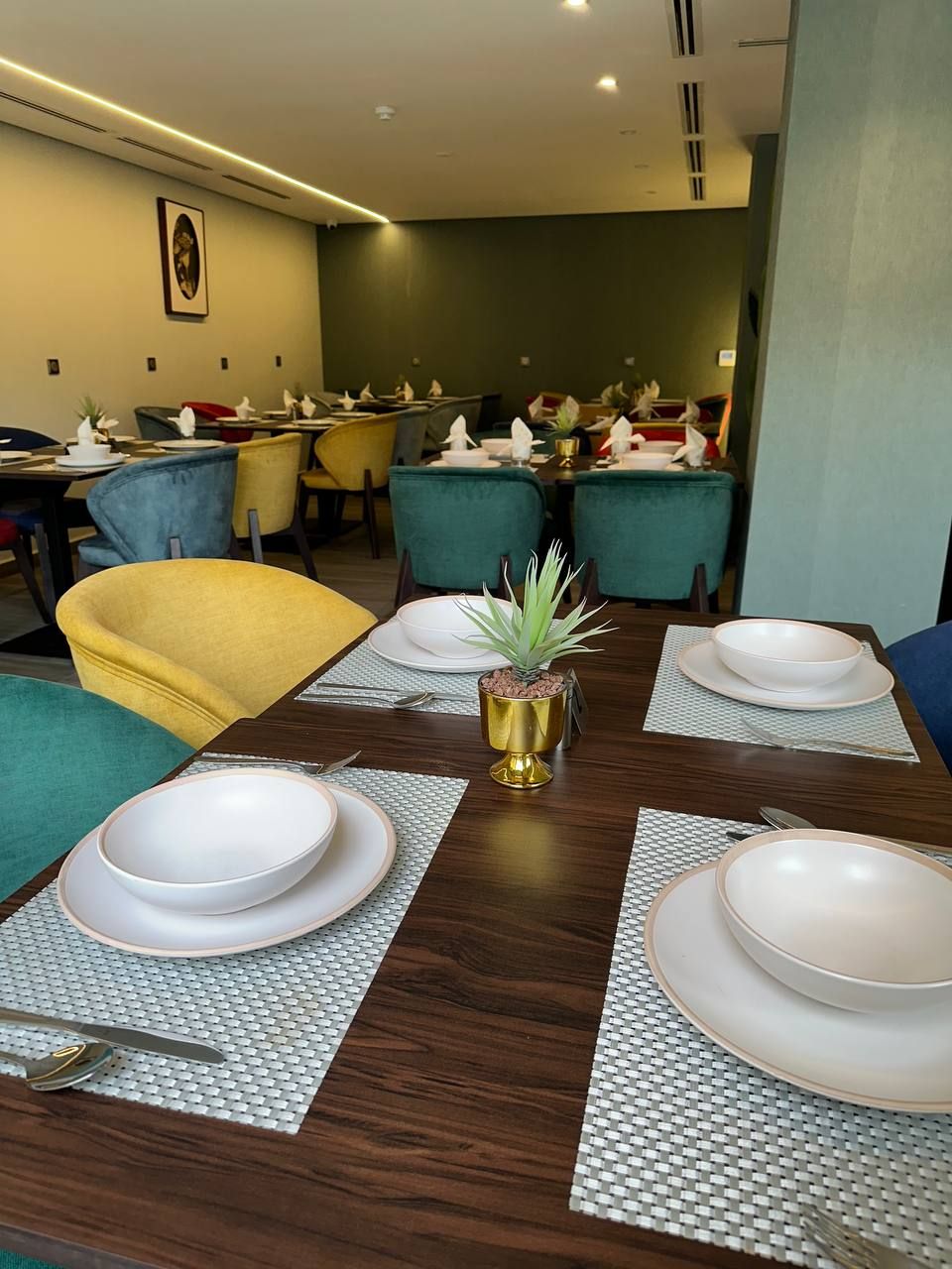 Un comedor con una larga mesa de madera dispuesta para una comida, rodeada de sillas color turquesa y amarillo.