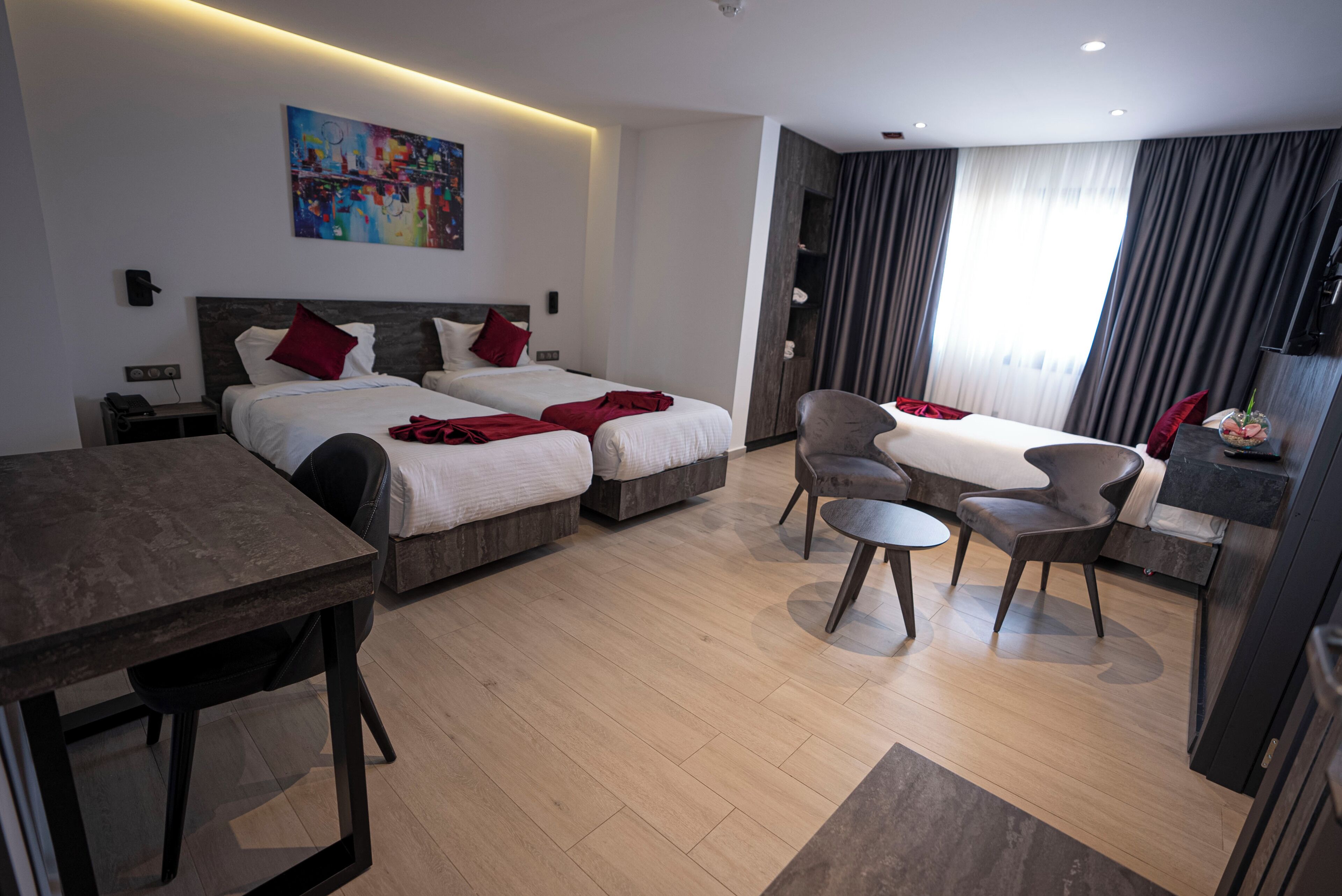 Habitación de hotel con dos camas, un escritorio y una silla. Hay un cuadro en la pared y una ventana con cortinas.