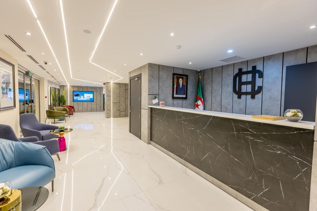 Uma área de recepção moderna com balcão de mármore, assentos e um painel digital.