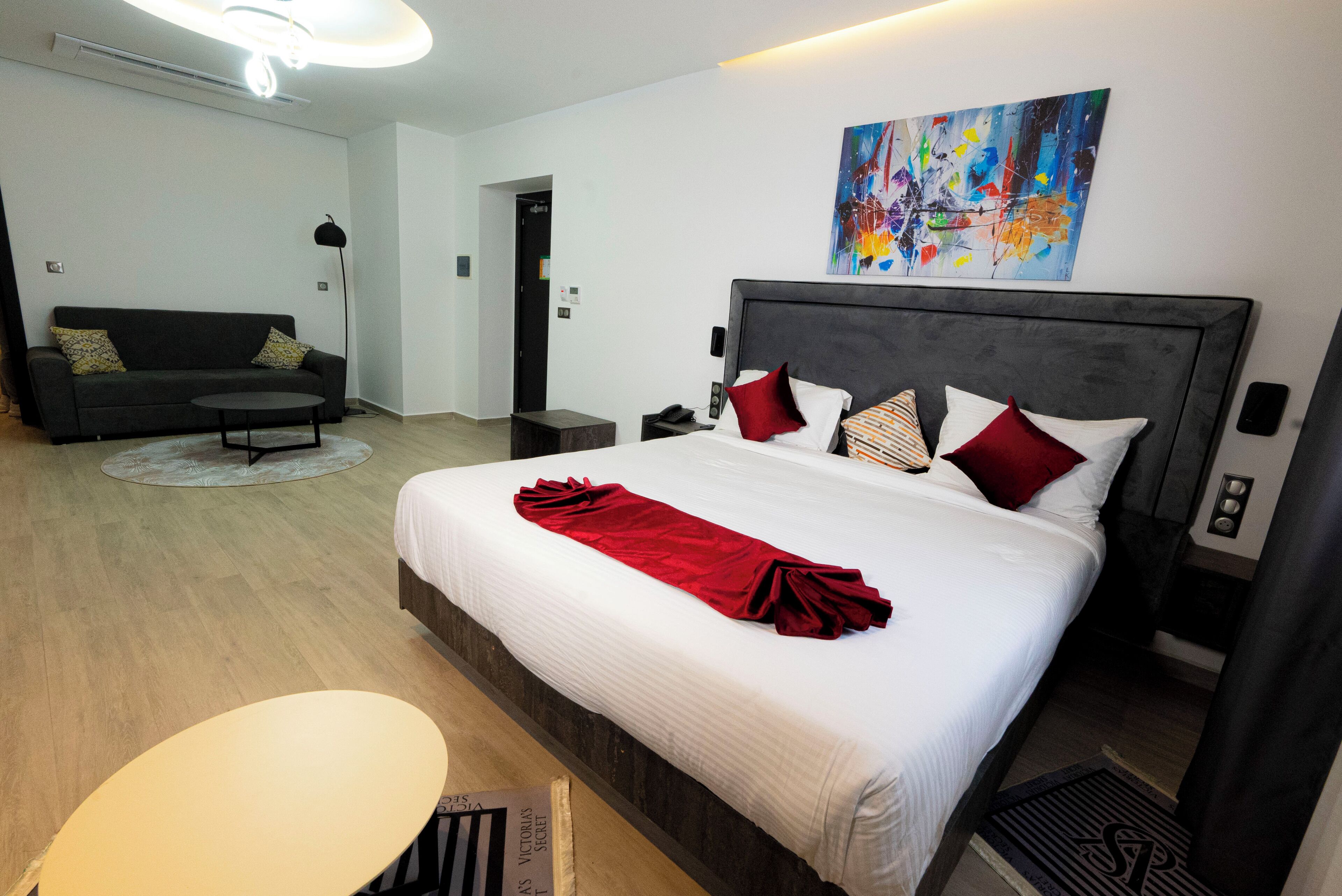 Una habitación de hotel moderna con una cama grande, un sofá, una mesita y un cuadro en la pared.