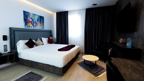 A modern hotel room with a large bed, a bedside table, a small round table, and a TV mounted on the wall. - Coast Hotel (Boumerdès)