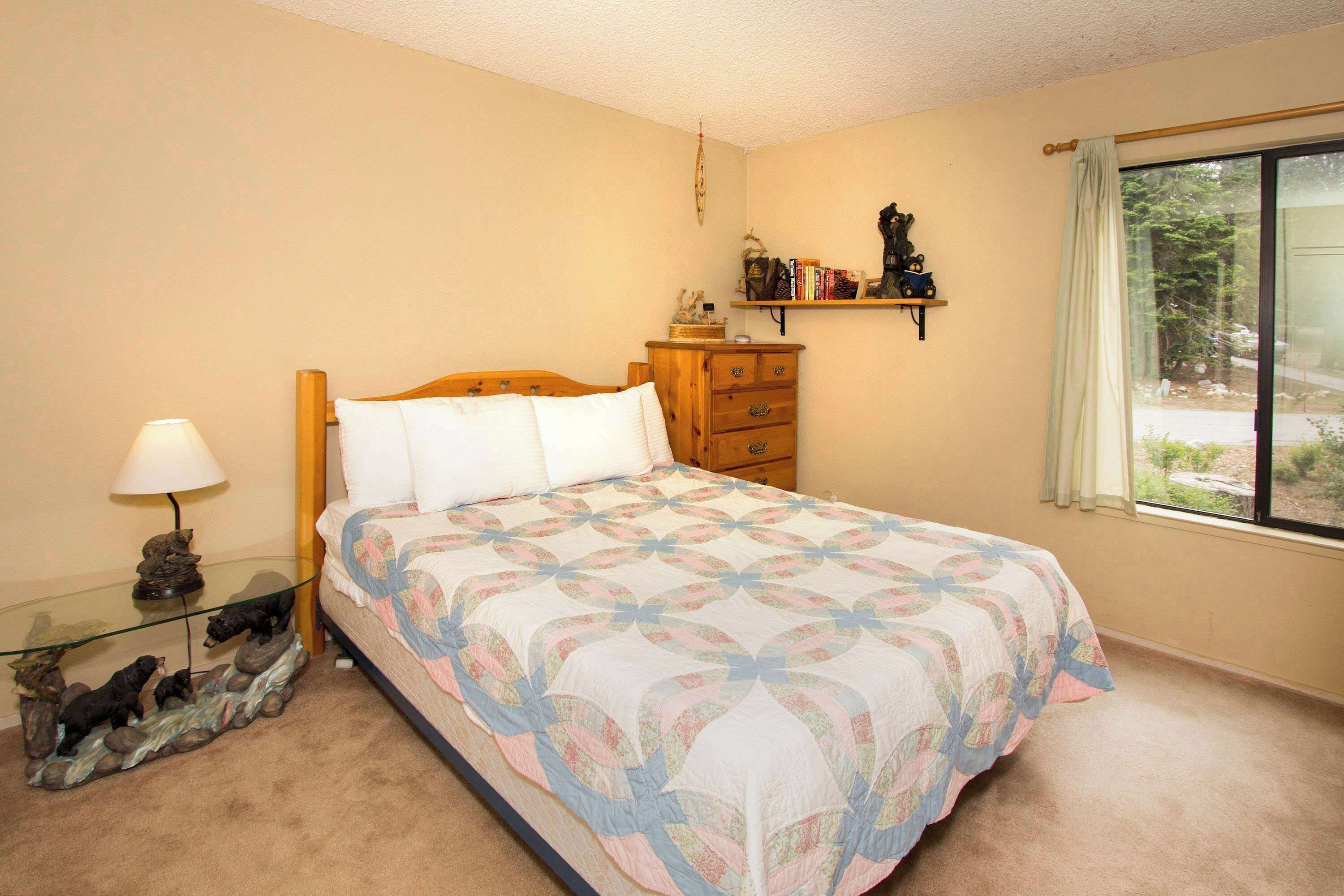 Une chambre à coucher comprenant un lit, une table de chevet, une commode, une étagère avec des livres et une fenêtre donnant sur un paysage agréable.