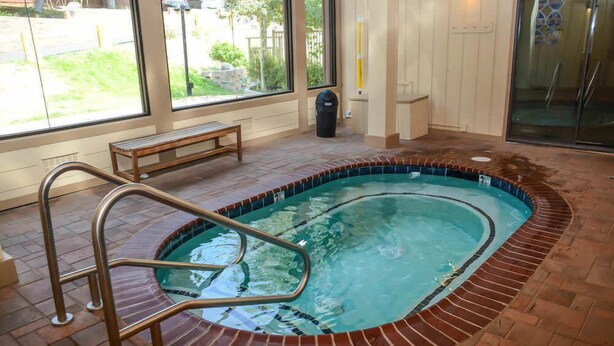 Une piscine intérieure équipée d’un escalier en métal, d’un banc en bois et offrant une vue sur l’extérieur grâce à de grandes fenêtres.