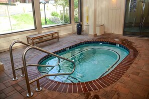 En indendørs swimmingpool med en metalstige, en træbænk og udsigt til det fri gennem store vinduer.
