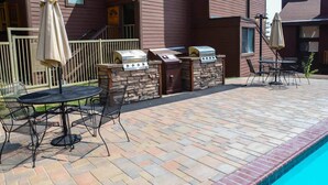 Une terrasse avec un barbecue en pierre, des sièges d’extérieur et une piscine.