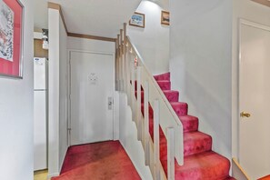 Un escalier recouvert d’une moquette rouge menant à une porte dotée d’un cadre blanc.