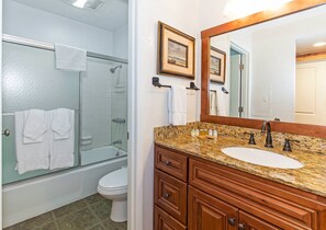 Een badkamer met een douchecabine van glas, een wit toilet en een wastafel met een granieten aanrechtblad en houten kastjes.