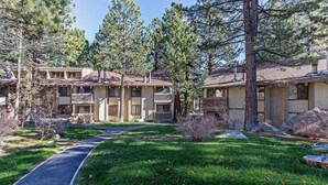 A two-story motel with a central walkway, surrounded by pine trees and a well-maintained lawn.