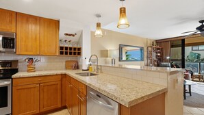 A kitchen with wooden cabinets, a granite countertop, stainless steel appliances, pendant lighting, and a view to the outside.