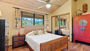 A bedroom with a wooden bed, a nightstand, a red cabinet, a ceiling fan, and a window with curtains.