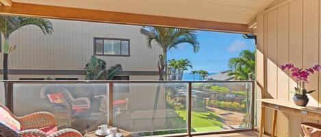 A balcony with wicker furniture, a potted orchid, and a view of a golf course and ocean.