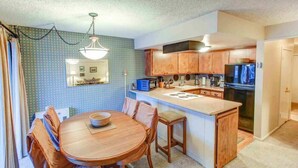 A kitchen with wooden cabinets, a central island, a dining table with chairs, and a hanging light fixture. - Fireside | Pool Access, Hot Tub & More (Mammoth Lakes)