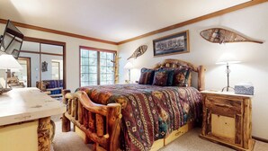 A bedroom with a wooden bed frame, a large window, a wooden desk, and a bedside table with a lamp. - Walk to Mammoth Ski Lifts | Ski Storage | Sleeps 6 (Mammoth Lakes)