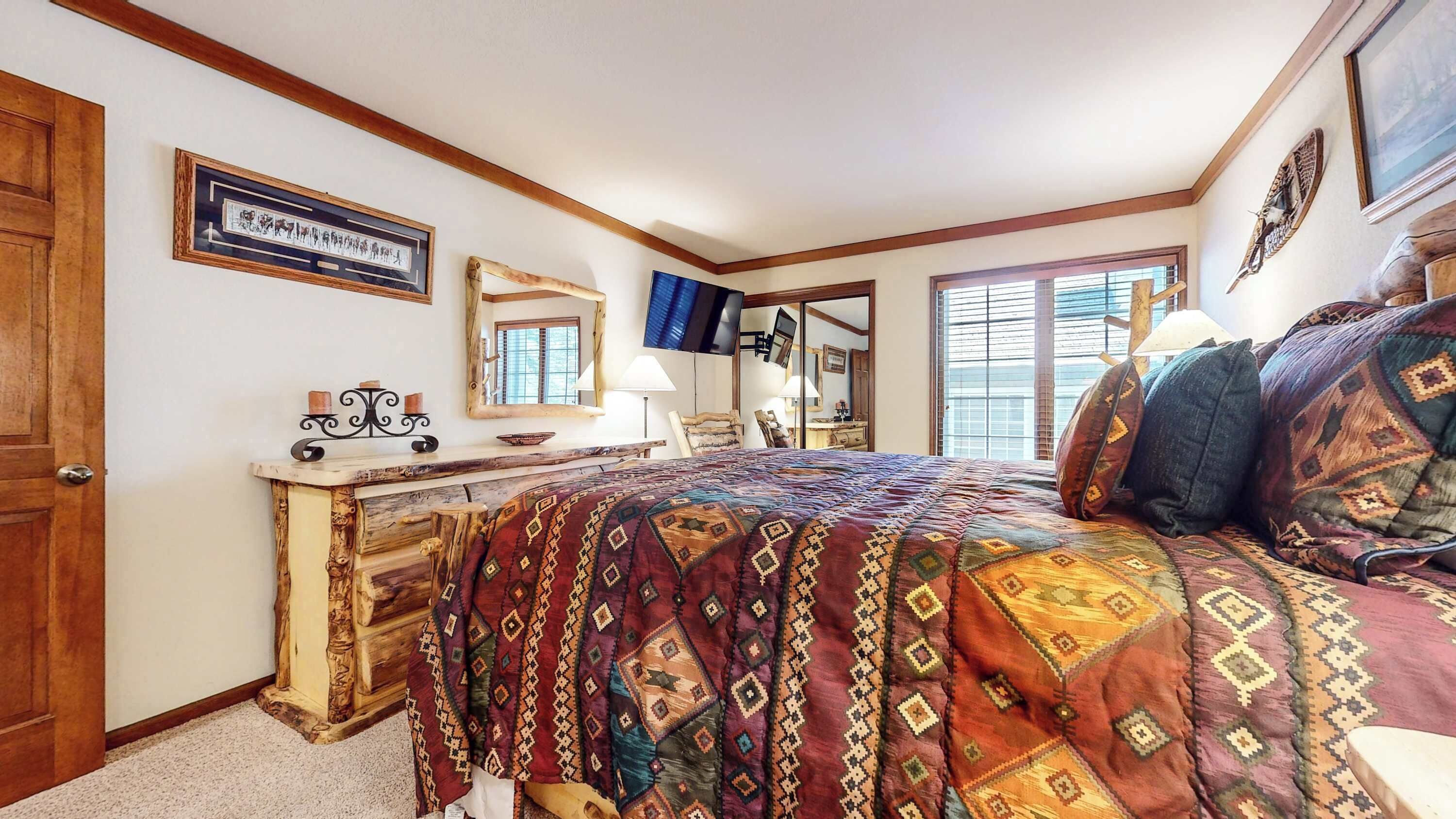 A bedroom with a large bed, a wooden dresser, a mirror, and a television.