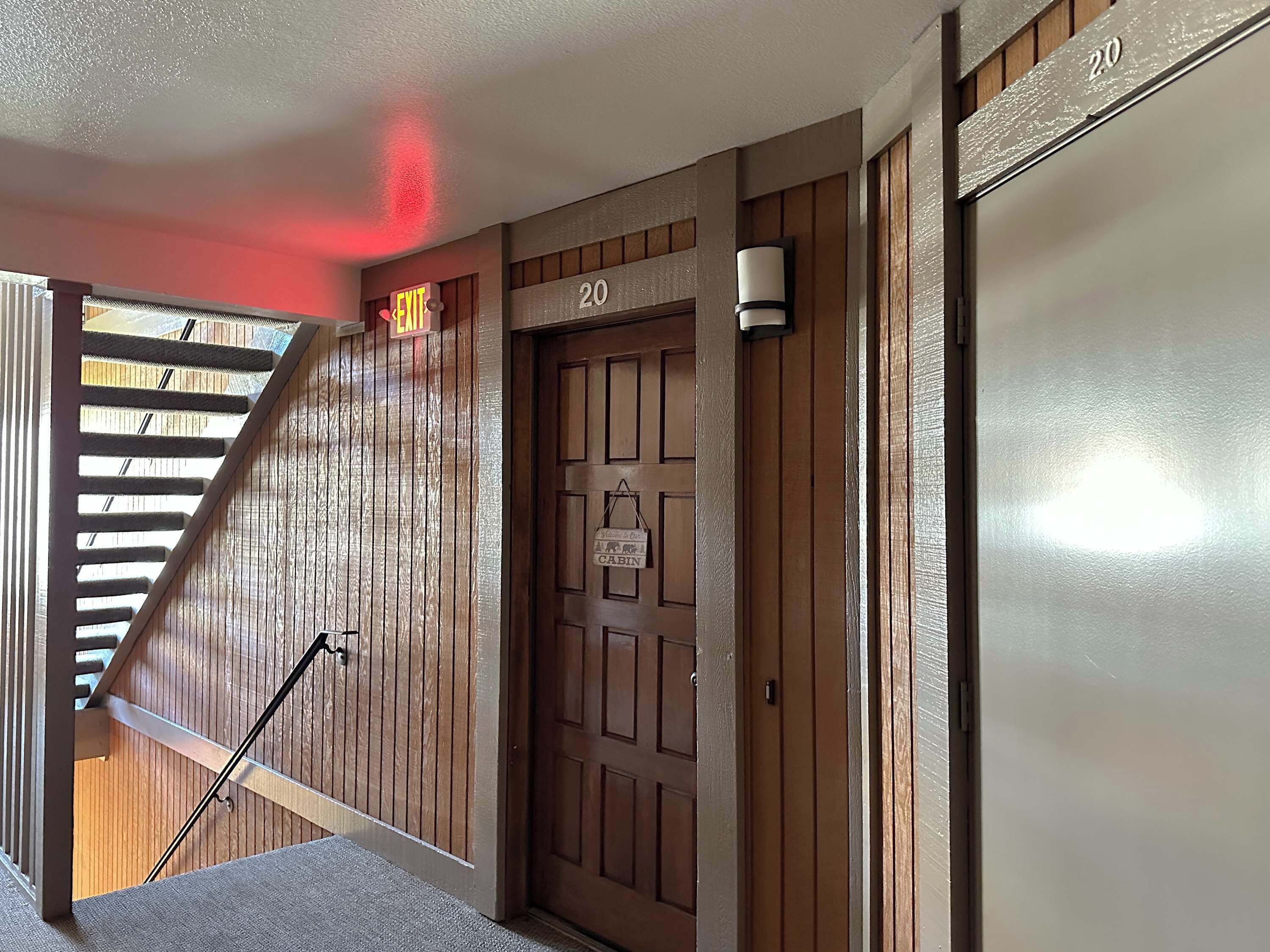 A wooden door with a sign indicating room number 20, a staircase with a handrail, and a wall-mounted light fixture.