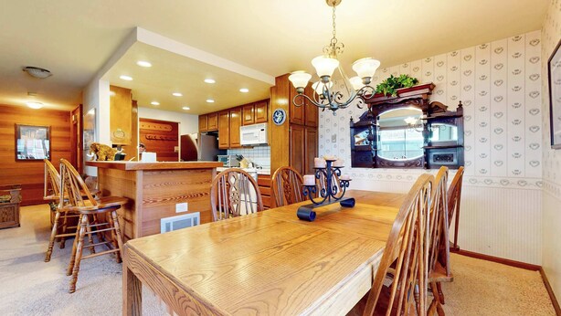 A dining area with a wooden table and chairs, a chandelier, and a kitchen in the background. - Walk to Mammoth Ski Lifts | Ski Storage | Sleeps 6 (Mammoth Lakes)