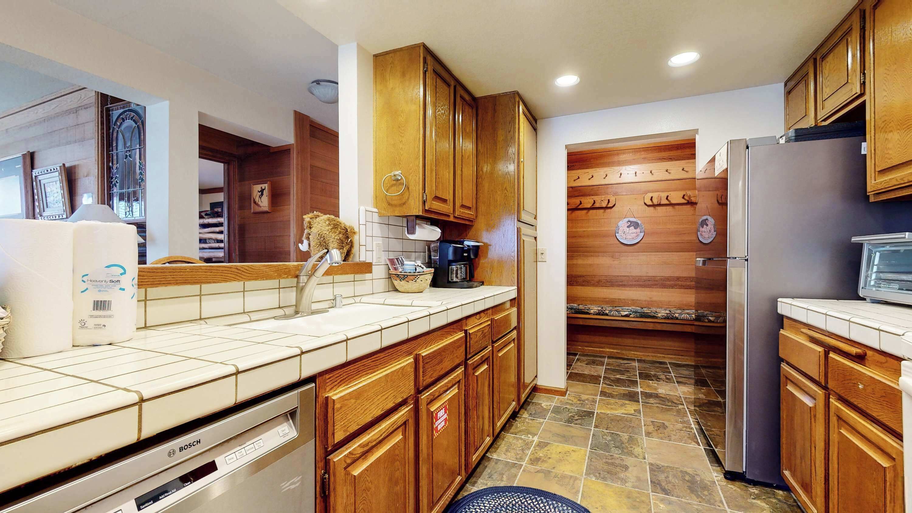 A kitchen with wooden cabinets, a Bosch dishwasher, a refrigerator, and a coffee maker.