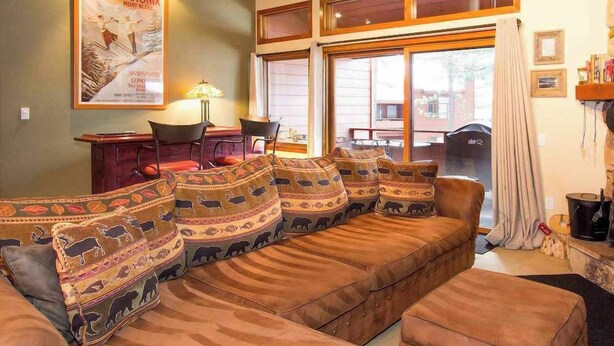Un salón acogedor con un sofá de cuero marrón decorado con estampados de animales, una mesa de centro de madera y un amplio ventanal con vistas al exterior.