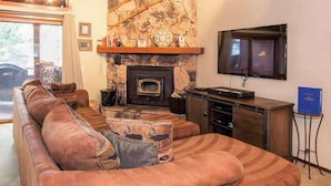Una sala de estar acogedora con chimenea de piedra, sofá de cuero y televisor de pantalla plana montado en la pared.