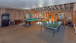 A spacious room with a pool table, ping pong table, and a retro arcade machine.
