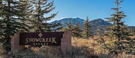 A sign for Snow Creek Resort surrounded by trees and mountains.
