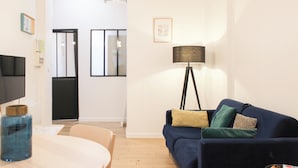 A modern living room with a dark blue sofa, a round wooden table, and a floor lamp. - Cozy apartment - close to Montmartre (Paris)