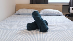 A neatly made bed with striped bedding and a rolled-up towel on top. - Cozy apartment - close to Montmartre (Paris)