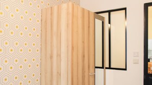 A wooden wardrobe with a mirror, a geometric patterned wall, and a black-framed window. - Cozy apartment - close to Montmartre (Paris)