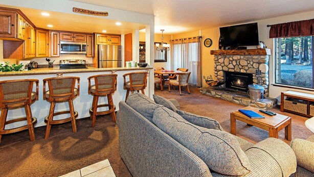 A cozy living room with a fireplace, a dining area, and a kitchen with wooden cabinets and a bar.