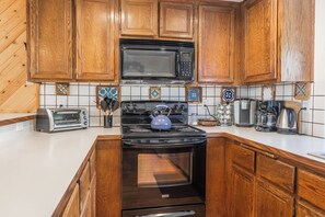 A kitchen with wooden cabinets, a black microwave, a stove with a kettle, a coffee maker, and a toaster.