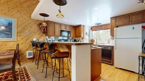 A kitchen with wooden cabinets, a central island with stools, a microwave, and a refrigerator. - Mins to Lodge & Ski Shuttle | Parking for 2 (Mammoth Lakes)