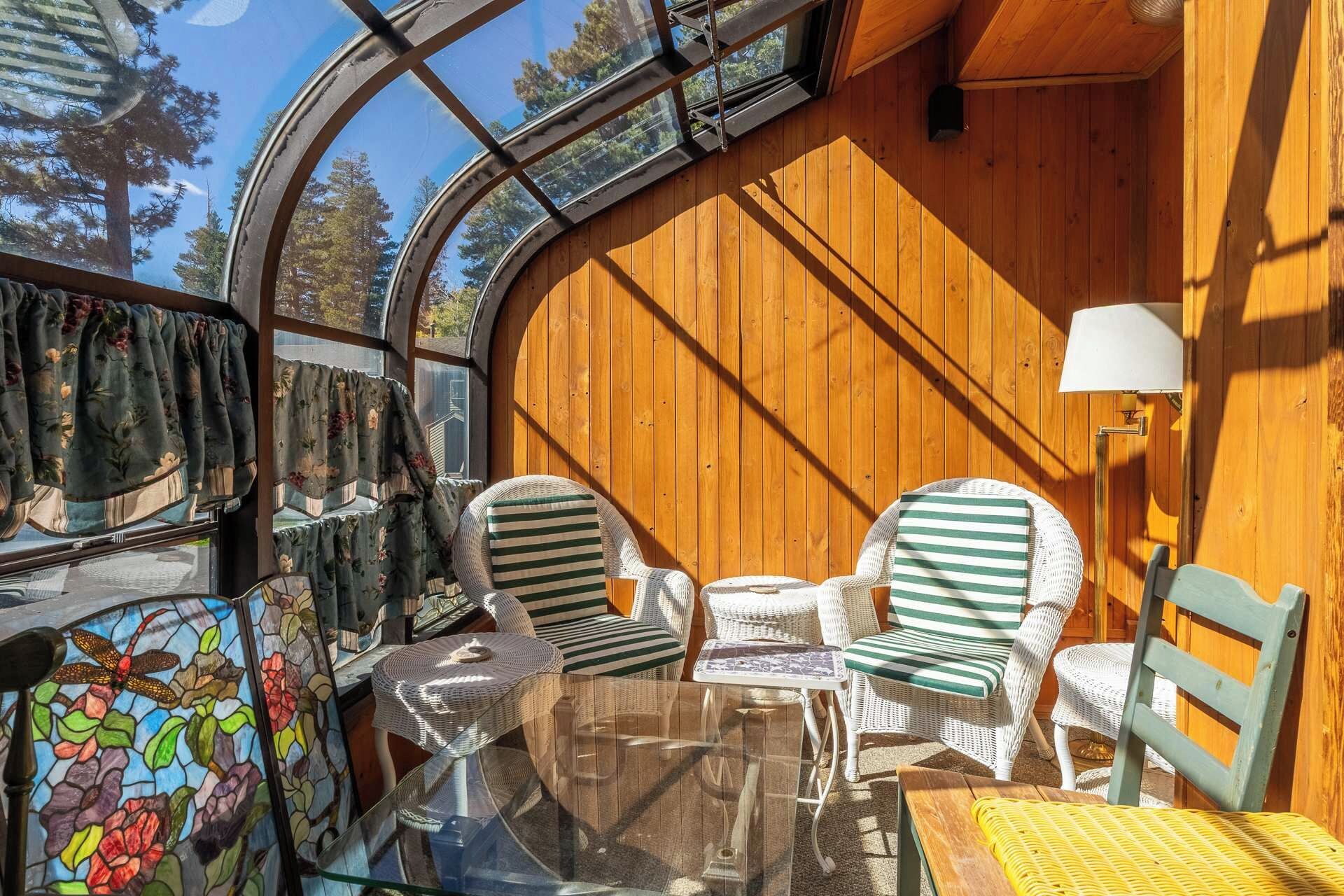 Une pièce chaleureuse avec un plafond en verre, des murs en bois, des meubles en osier et une table.