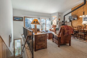 A cozy living room with a fireplace, wooden furniture, and a view of the outdoors.