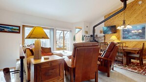 A cozy living room with a fireplace, leather chairs, a wooden dining table, and a large TV mounted on the wall. - Mins to Lodge & Ski Shuttle | Parking for 2 (Mammoth Lakes)