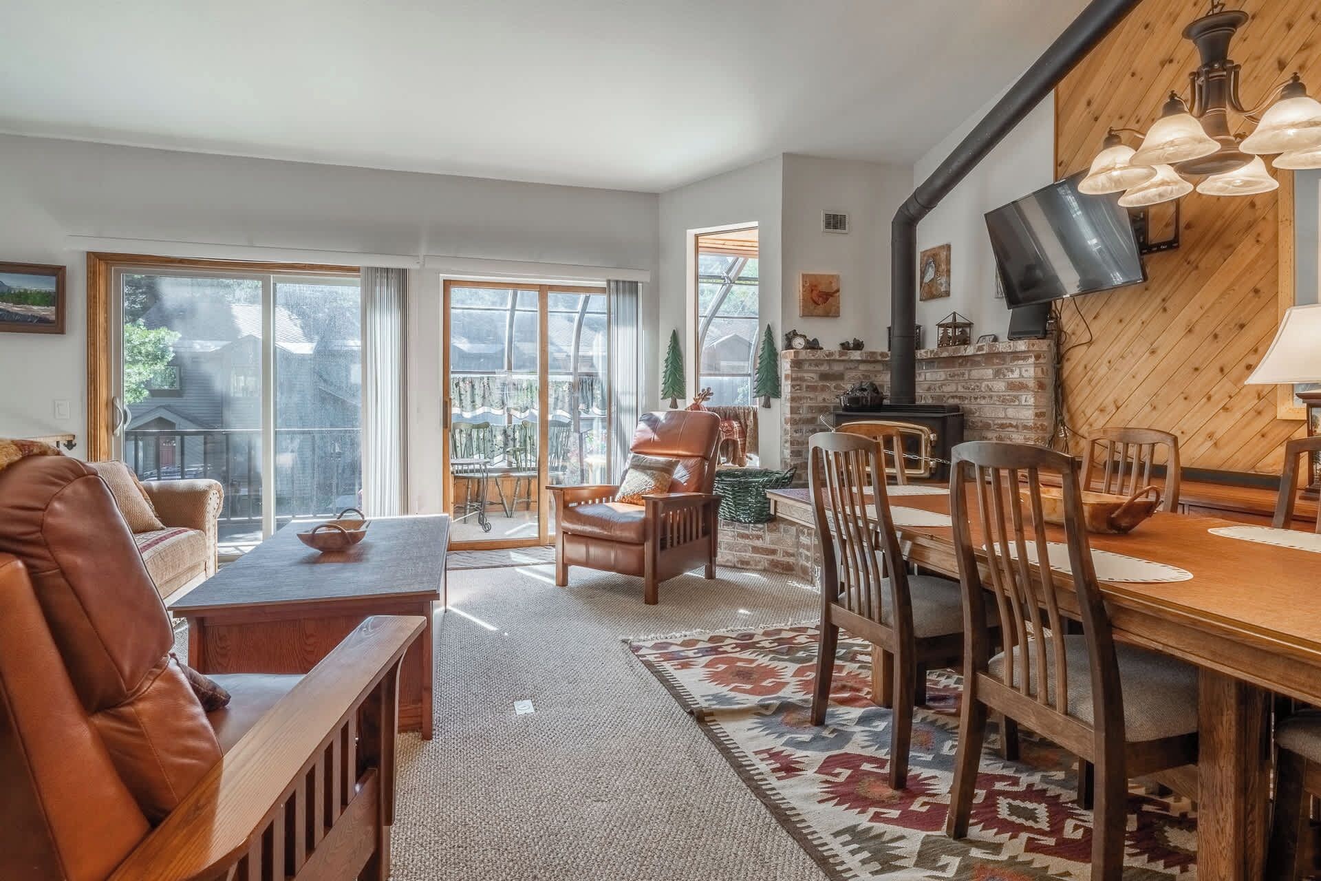 A cozy living room with a fireplace, large windows, and a dining area with wooden furniture.