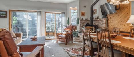 A cozy living room with a fireplace, large windows, and a dining area with wooden furniture.