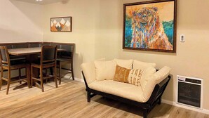 A dining area with a wooden table and chairs, a beige sofa with patterned cushions, and a large painting of a bear on the wall. - Sierra Manors #098 | Nearby Hike/Bike Trails (Mammoth Lakes)
