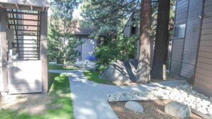 A residential property with a paved driveway, a stone pathway, and a small garden area with rocks and grass. - Sierra Manors #098 | Nearby Hike/Bike Trails (Mammoth Lakes)
