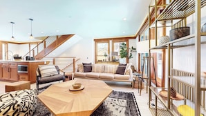 Un espacio habitable moderno con una mesa de comedor de madera, un sofá, una zona de cocina y una escalera.