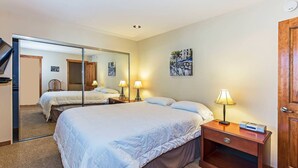 A hotel room with two beds, a large mirror, a wooden dresser, and a desk with a lamp and a clock.